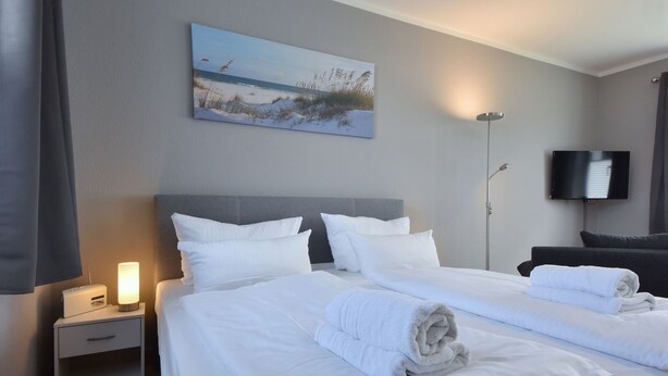 A hotel room with two beds, a nightstand with a lamp, a flat-screen TV, and a painting of a beach scene on the wall.