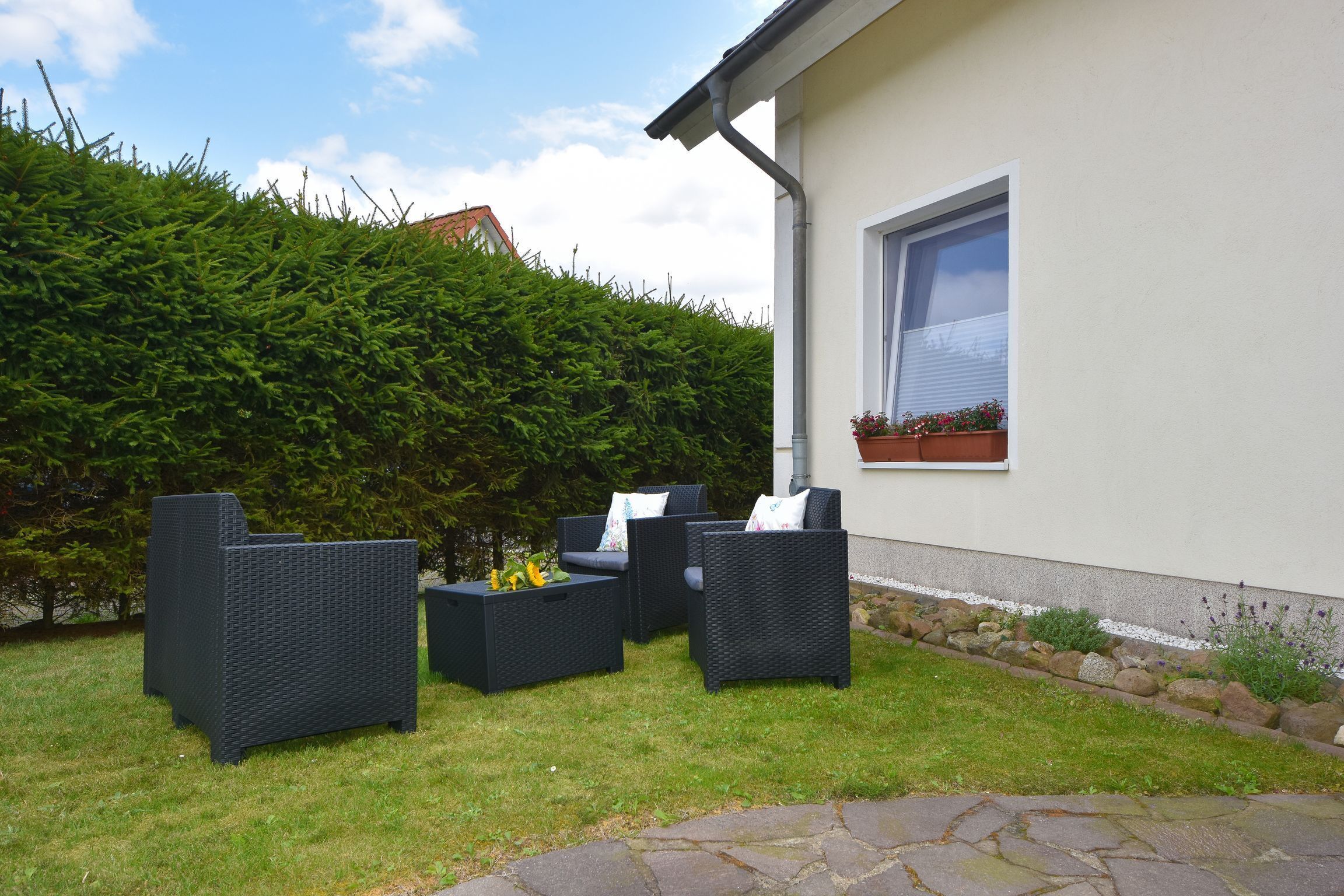 Ein Sitzbereich im Freien mit Korbmöbeln, einem Steinweg und einer Hecke.