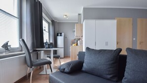 A modern living room with a dark grey sofa, a dining area with a table and chairs, and a kitchen with cabinets and a microwave.