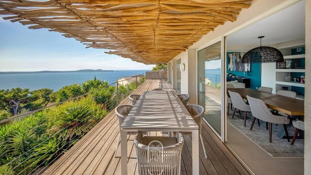 Un terrazzo in legno con tavolo e sedie, affacciato su una vista panoramica del mare.