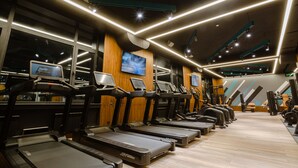 Un gimnasio con cintas de correr, máquinas de ejercicio y una gran pantalla de televisión.