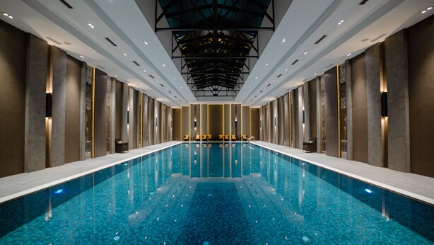 Una piscina interior moderna con un diseño geométrico en el techo e iluminación uniforme.