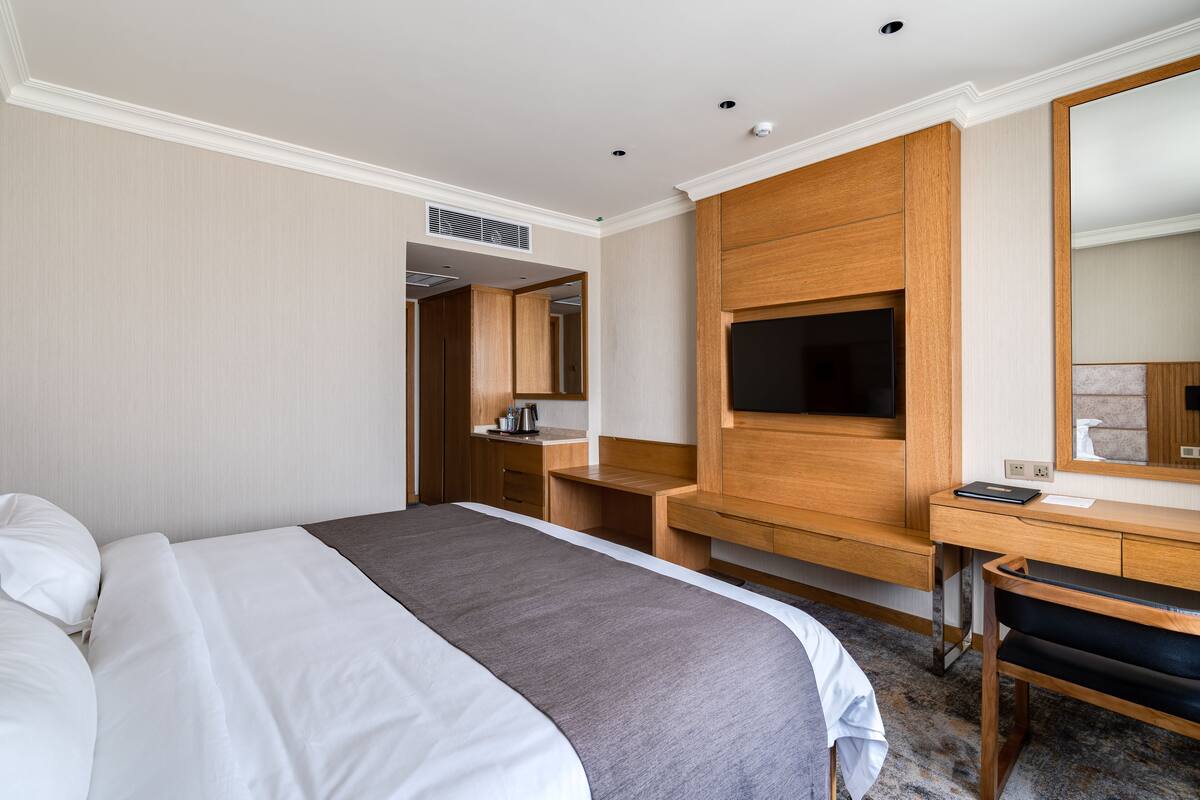 A hotel room with a large bed, a wooden desk, a flat-screen TV, and a mirror.
