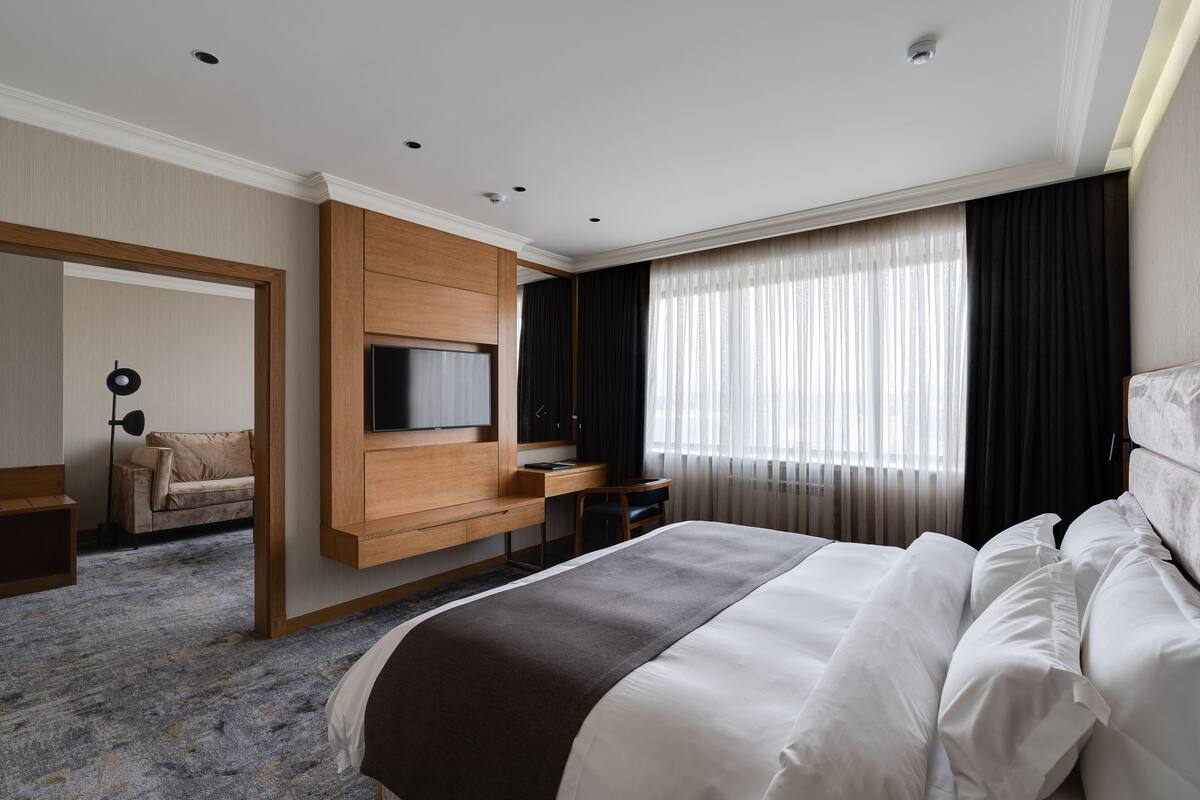 A modern hotel room with a large bed, a flat-screen TV mounted on the wall, a desk, and a sofa.