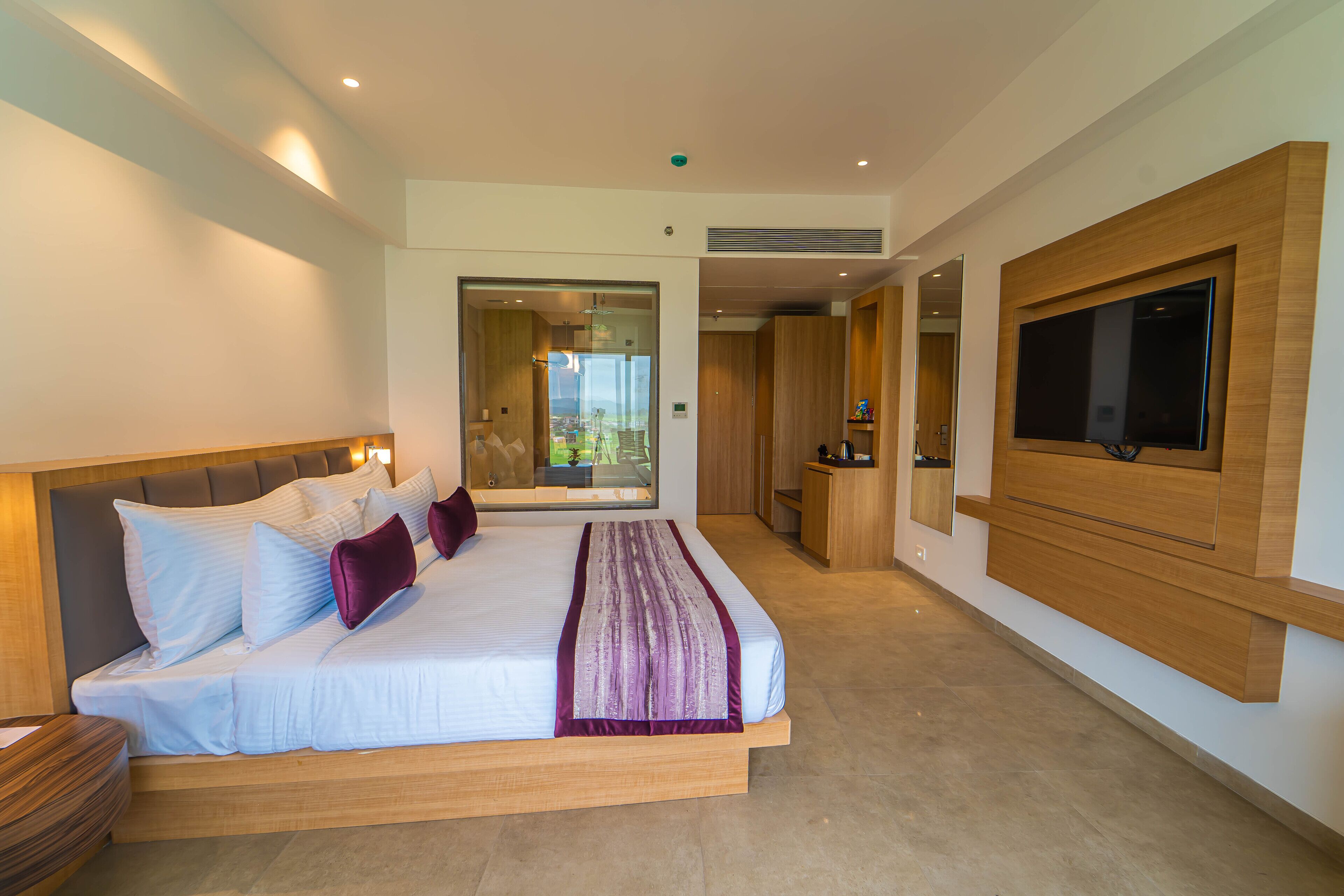 A modern hotel room with a large bed, a TV mounted on the wall, and a view of the outdoors.