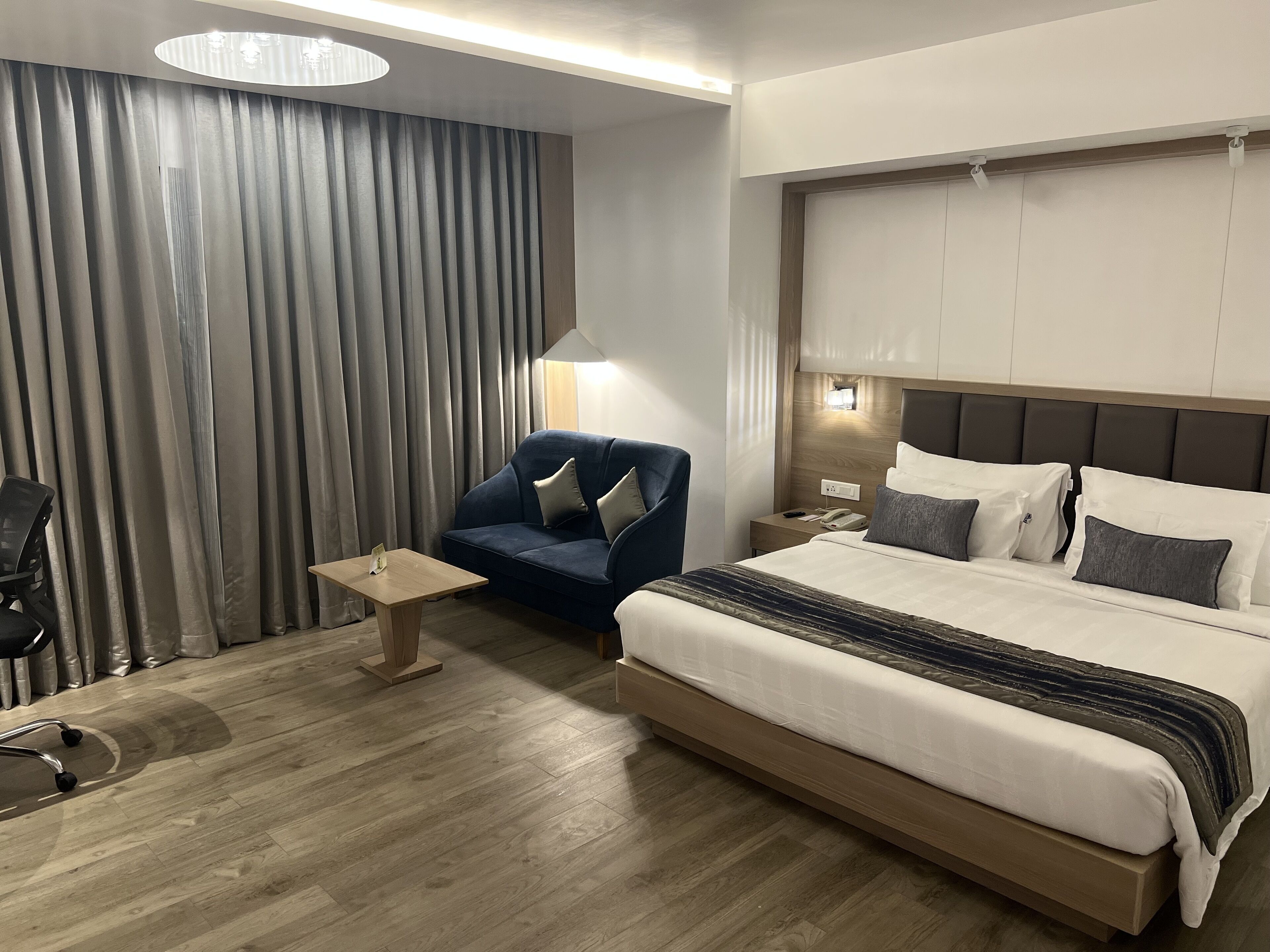 Habitació d'hotel amb un llit gran, una taula de treball, una cadira i una cortina.
