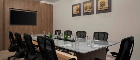 A conference room with a long table, black chairs, a flat-screen TV, and three framed artworks on the wall.