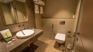 Un baño moderno con encimera de granito, un lavabo blanco, un inodoro y ducha con mampara de cristal.