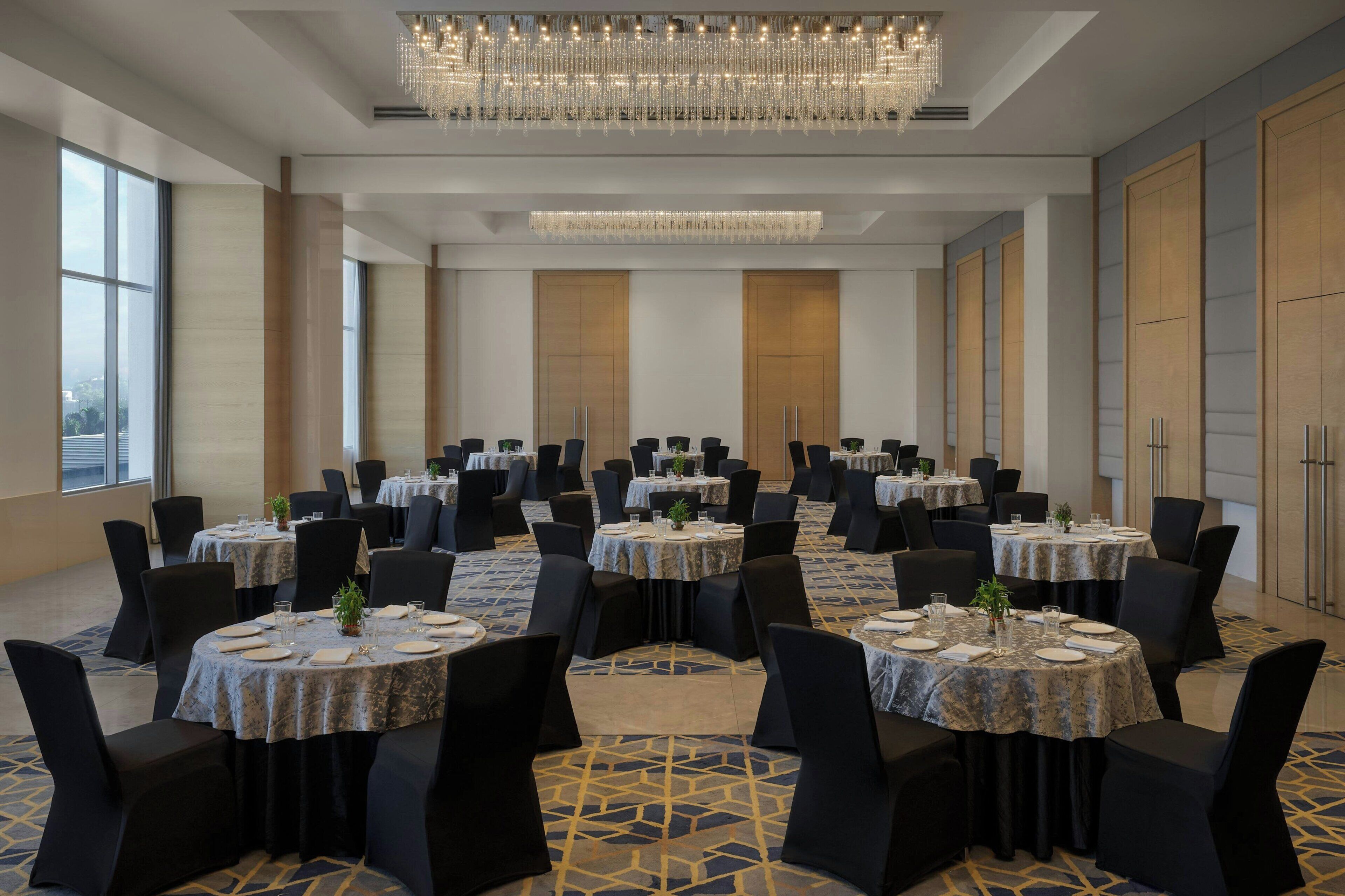 A conference room with multiple tables and chairs, large windows, and a chandelier.