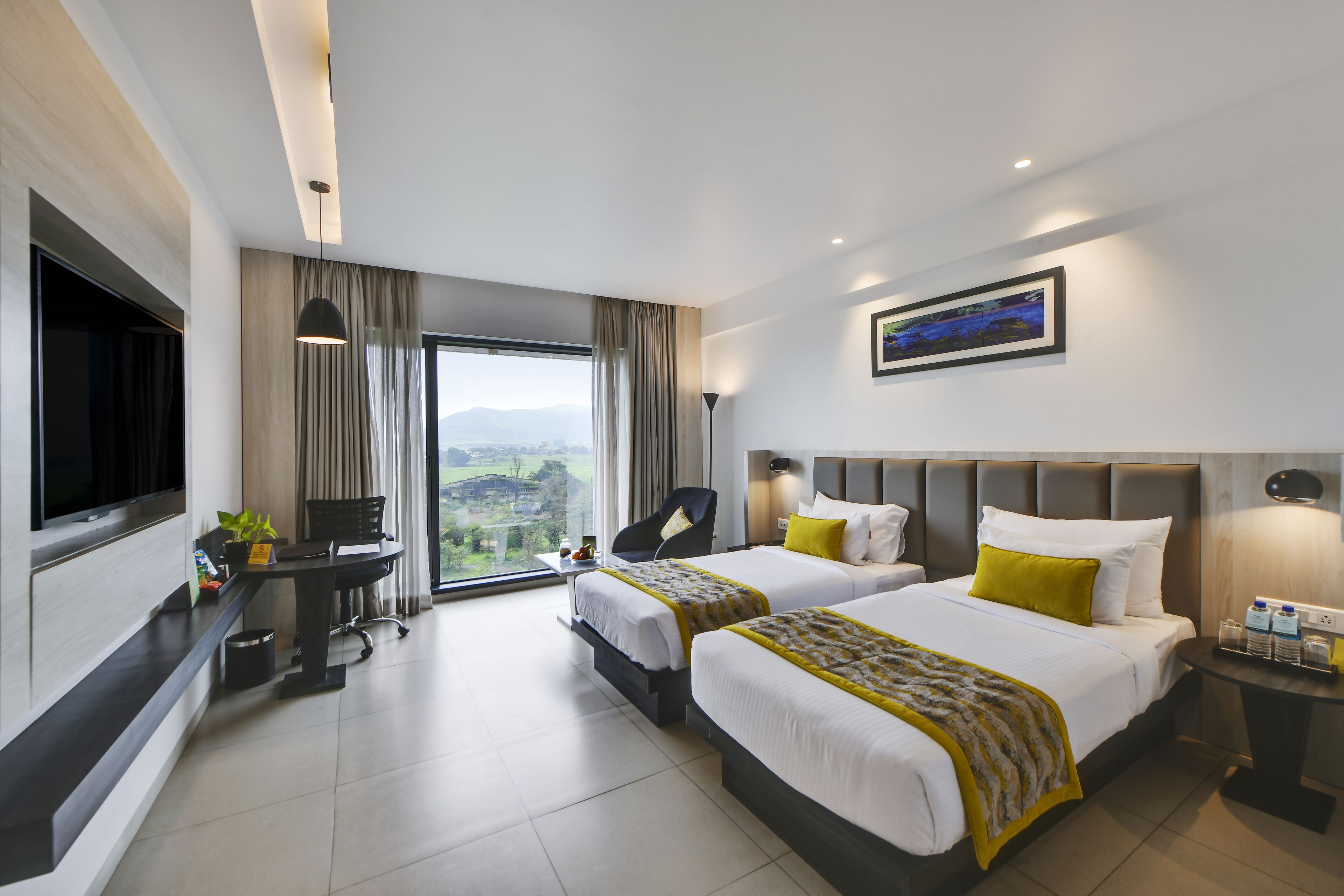 A hotel room with two beds, a desk, a chair, a TV, and a large window with a view.