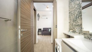 Une salle de bain moderne équipée d’un lave-linge intégré, d’un grand miroir et d’un espace douche.