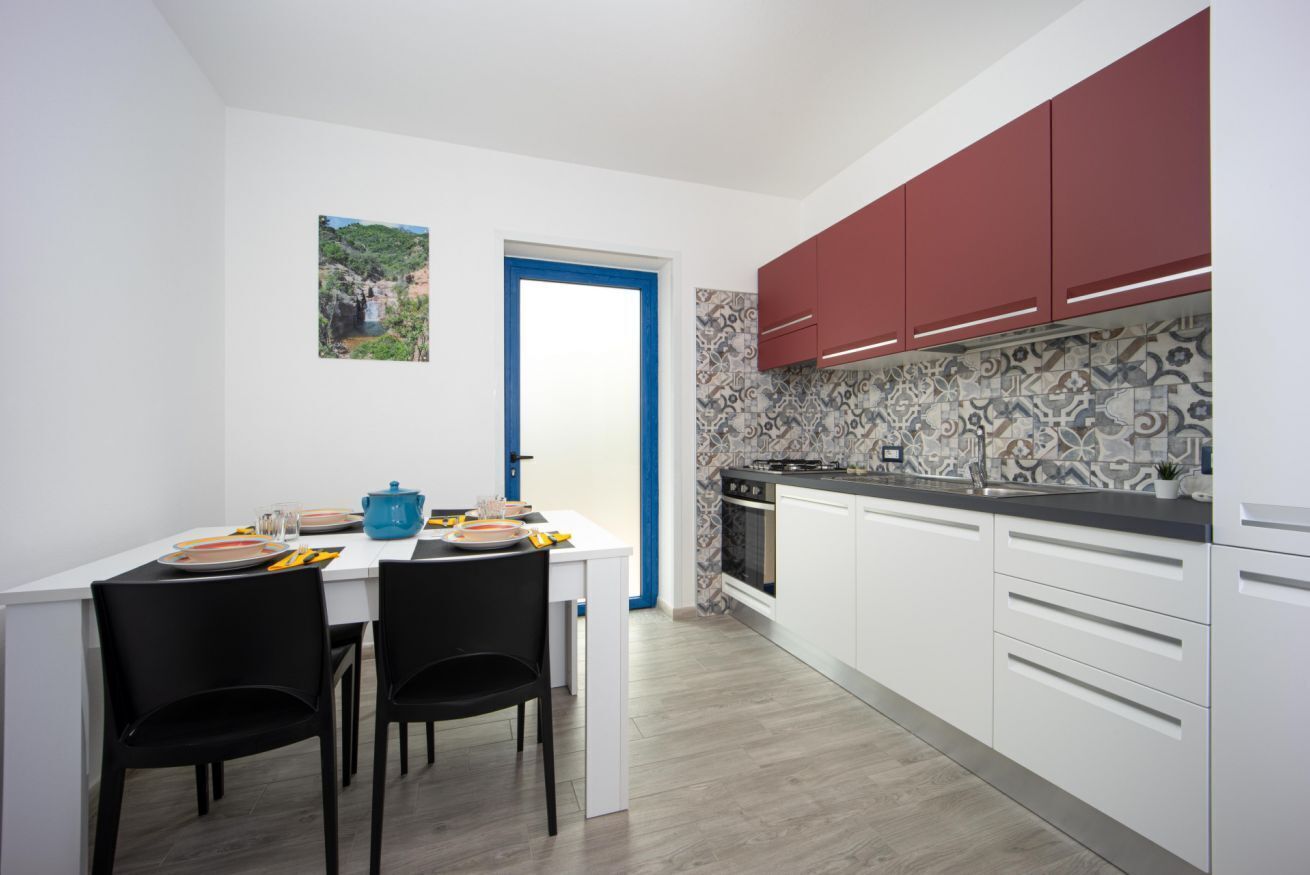 Une cuisine moderne avec des meubles blancs, un meuble supérieur rouge, un pare-feu décoré et un coin repas avec une table blanche et des chaises noires.