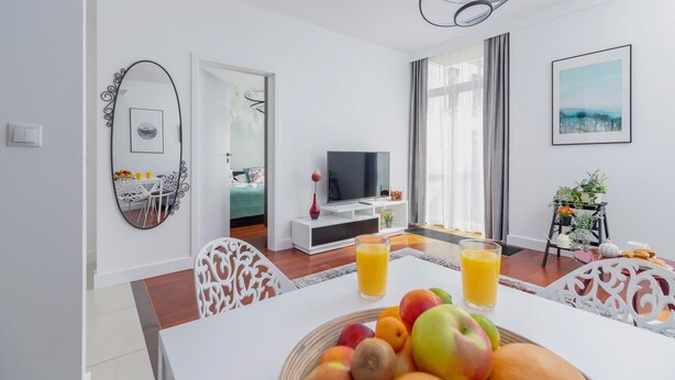 Un salon moderne avec une table à manger, des chaises, un téléviseur et un panier de fruits.