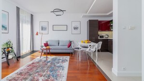 Un salon moderne avec un canapé gris, une table à manger avec des chaises, et une cuisine en arrière-plan.