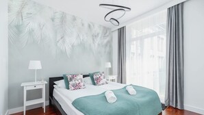 Une chambre à coucher moderne avec un lit, des tables de chevet, une couverture verte et un mur orné d’un motif de feuilles.