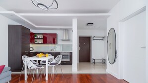 Une cuisine moderne avec des meubles blancs, un mur d’accent rouge et un coin repas comprenant une table et des chaises blanches.