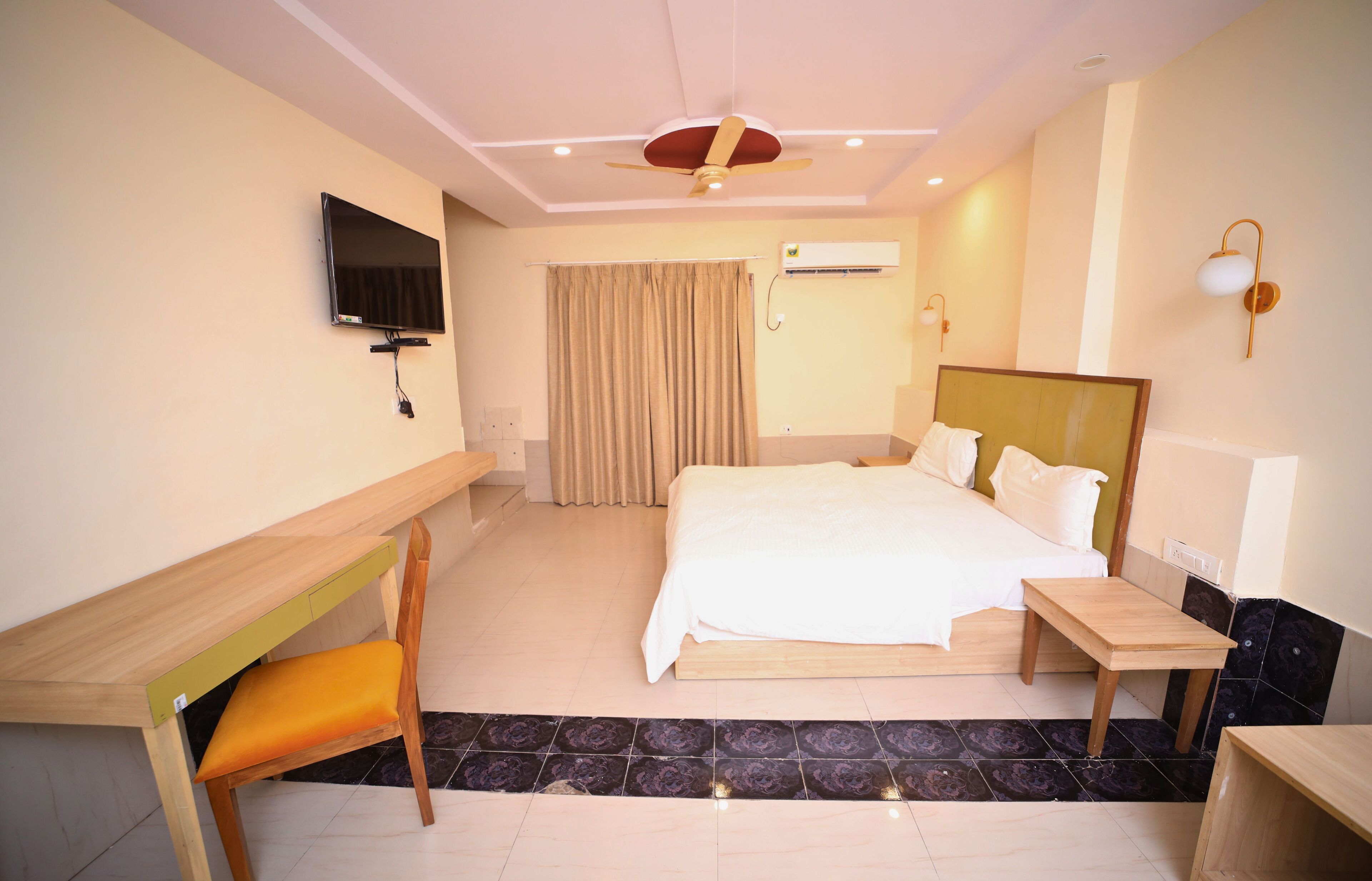 A hotel room with a bed, a desk, a chair, a TV, and a ceiling fan.