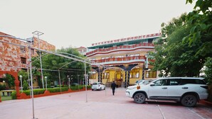 A multi-story building with a red and yellow facade, a covered walkway, and parked cars. - Kenth Hari Resort Dhaulpur by ShriGo Hotels (Dhaulpur)