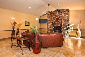 A lobby with a stone fireplace, leather sofa, and a large vase with plants.