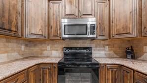 A kitchen with wooden cabinets, a stainless steel microwave, and a black stove. - Ground Level Heavenly Suite | Private BBQ Patio (Hurricane)