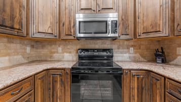 A kitchen with wooden cabinets, a stainless steel microwave, and a black stove.
