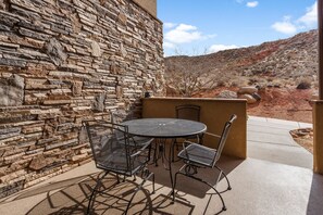 Un patio con un muro de piedra, una mesa redonda y sillas de metal.