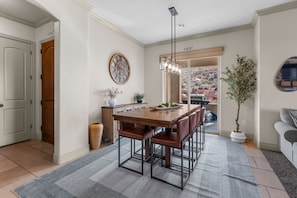 Comedor con mesa de madera, sillas metálicas, lámpara colgante y planta en maceta.