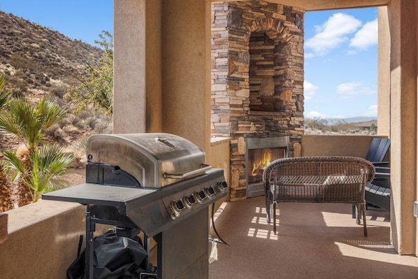 Un patio al aire libre con chimenea de piedra, una parrilla y una silla de mimbre.