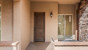 A beige exterior wall with a wooden door marked with the number 7, a stone wall, and a metal chair on a ledge. - Ground Level Heavenly Suite | Private BBQ Patio (Hurricane)