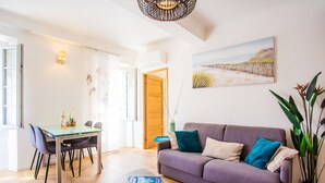 A modern living room with a dining area, a purple sofa, and a large window. - PARADISIO 2 AP4237 By Riviera Holiday Homes (Niza)