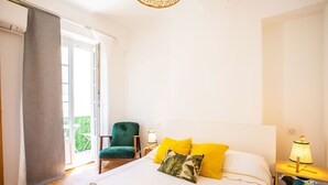 A hotel room with a bed, a chair, a nightstand, and a window. - PARADISIO 2 AP4237 By Riviera Holiday Homes (Niza)
