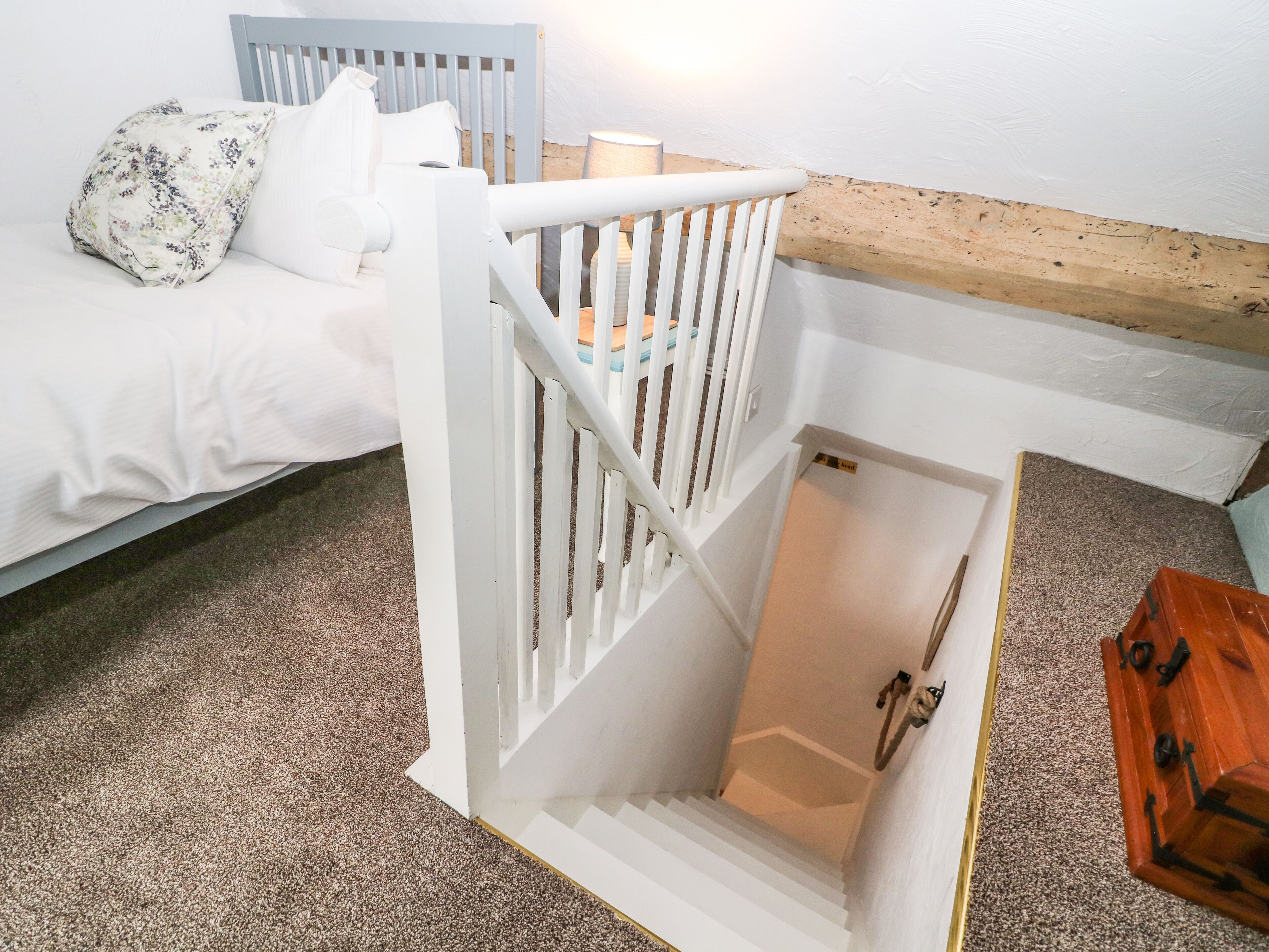 A bedroom with a bed, a white crib, a wooden bench, and a carpeted floor.