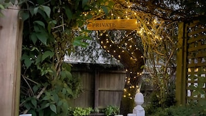 A white picket fence with a 'PRIVATE' sign and 'Tuesday Cottage' sign above it, surrounded by greenery and string lights. - Tuesday Cottage (Cheltenham)