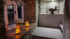 A cozy room with a stone wall, a window with a view of a statue, and three lit candles on a wooden shelf. - Tuesday Cottage (Cheltenham)
