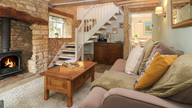 A cozy living room with a stone wall, a fireplace, a wooden staircase, and a comfortable sofa. - Tuesday Cottage (Cheltenham)