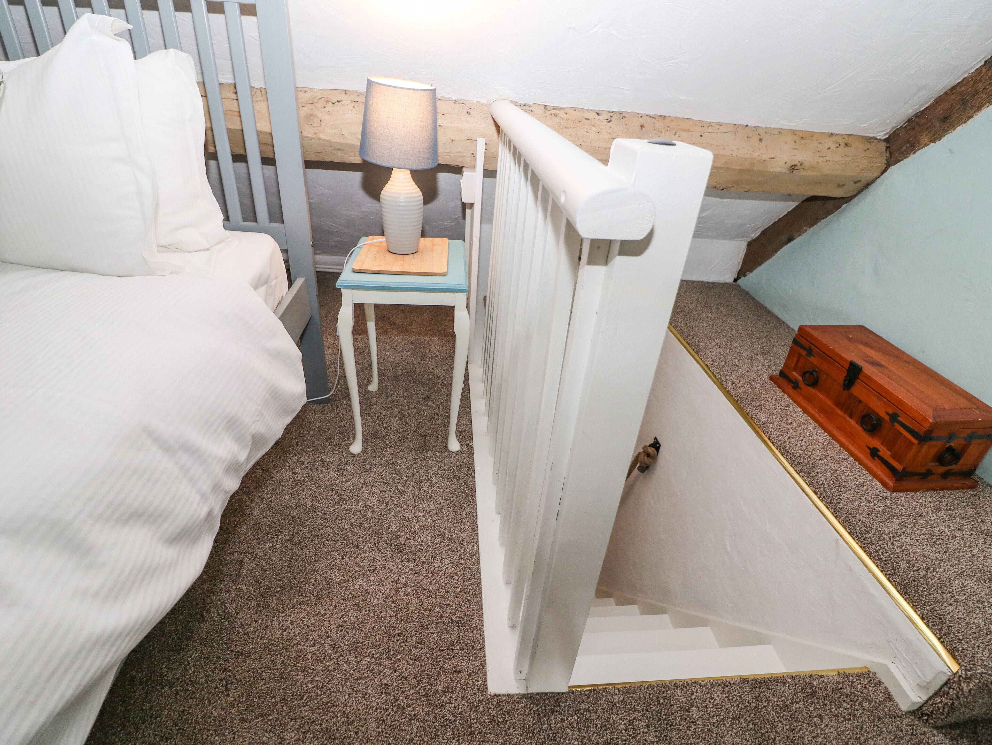A bedroom with a bed, a small table with a lamp, a radiator, and a wooden chest.