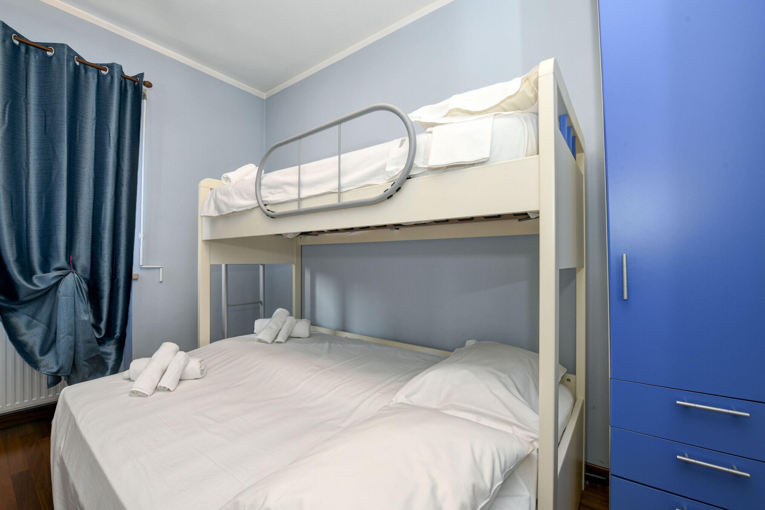 Ein Etagenbett mit weißer Bettwäsche und einem blauen Kleiderschrank.