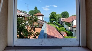 Blick aus einem Fenster auf eine Küstenlandschaft mit terrassenförmig angelegten Häusern, einem klaren Himmel und einer Wasserfläche in der Ferne.