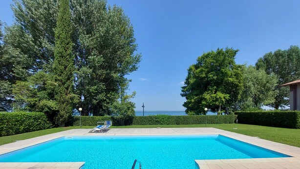 Ein rechteckiger Pool mit abgerundeter Kante, umgeben von einer gefliesten Terrasse. Auf der Terrasse stehen zwei Liegestühle und ein kleiner Tisch.