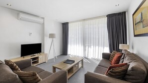 A modern living room with a flat-screen TV, a floor lamp, and a sofa with striped cushions. - Resort Apartment 224 (TORQUAY)