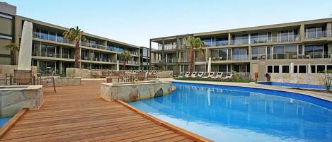 Un hôtel doté d’une piscine, d’une terrasse en bois et de plusieurs balcons.