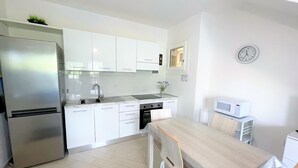 A modern kitchen with white cabinets, a stainless steel refrigerator, a microwave, and a wooden dining table with chairs. - Affittimoderni Viddalba Bouganville - VIBO09 (Viddalba)