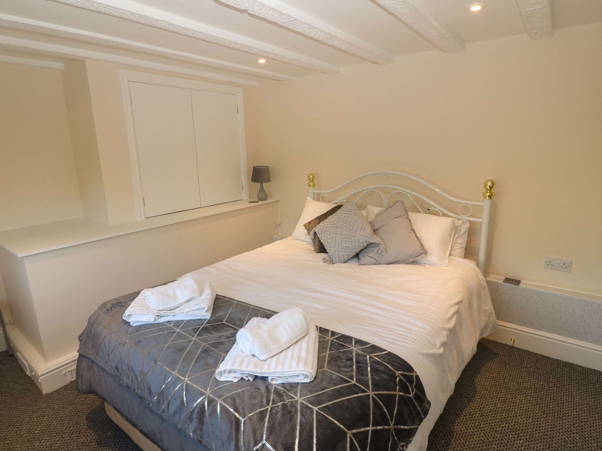 A neatly made bed with a geometric-patterned duvet, a bedside lamp, and a wall-mounted shelf with a lamp.