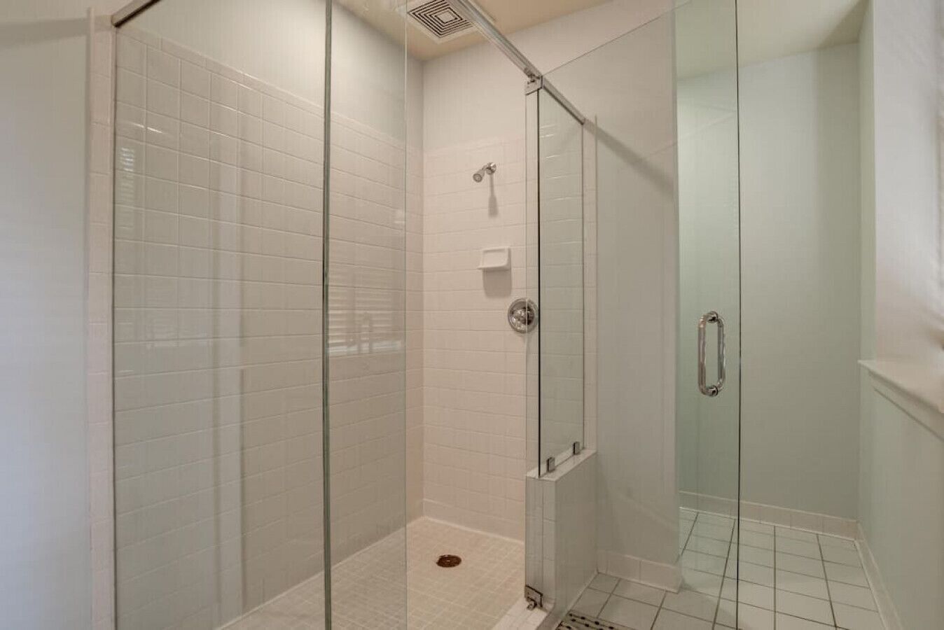 Ducha con cerramiento de vidrio, paredes de azulejos blancos y un tirador de metal.