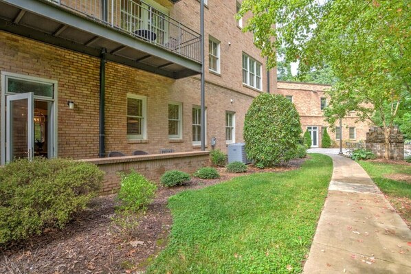 A brick building with a balcony, a well-maintained lawn, and a pathway leading to the entrance.