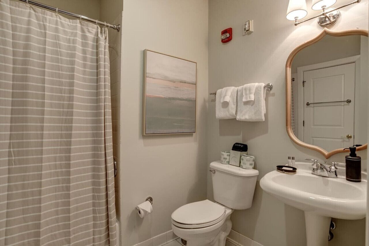 A bathroom with a shower curtain, toilet, sink, and a framed picture on the wall.
