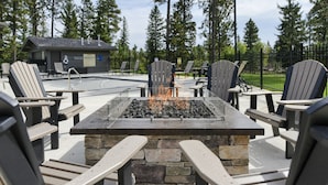 Un espacio al aire libre con sillas tipo Adirondack, un hogar a leña de piedra y un área de descanso junto a la piscina.