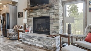 Una chimenea de piedra con un televisor de pantalla plana encima, un banco de madera y un sofá con un cojín rojo.