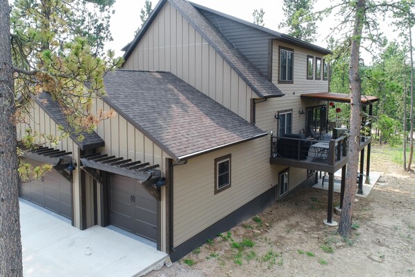 A two-story house with a garage, a covered porch, and a deck. - 3 Level Cabin w/ Large Driveway on Paved Roads Close to Attractions! Hot Tub! (Lead)