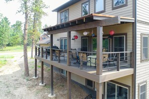 A two-story building with a covered deck area featuring outdoor seating and a grill. - 3 Level Cabin w/ Large Driveway on Paved Roads Close to Attractions! Hot Tub! (Lead)